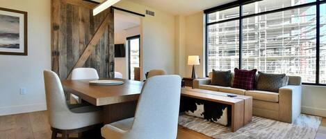 Una sala de estar moderna con comedor, ventanas amplias y vista a una obra en construcción.