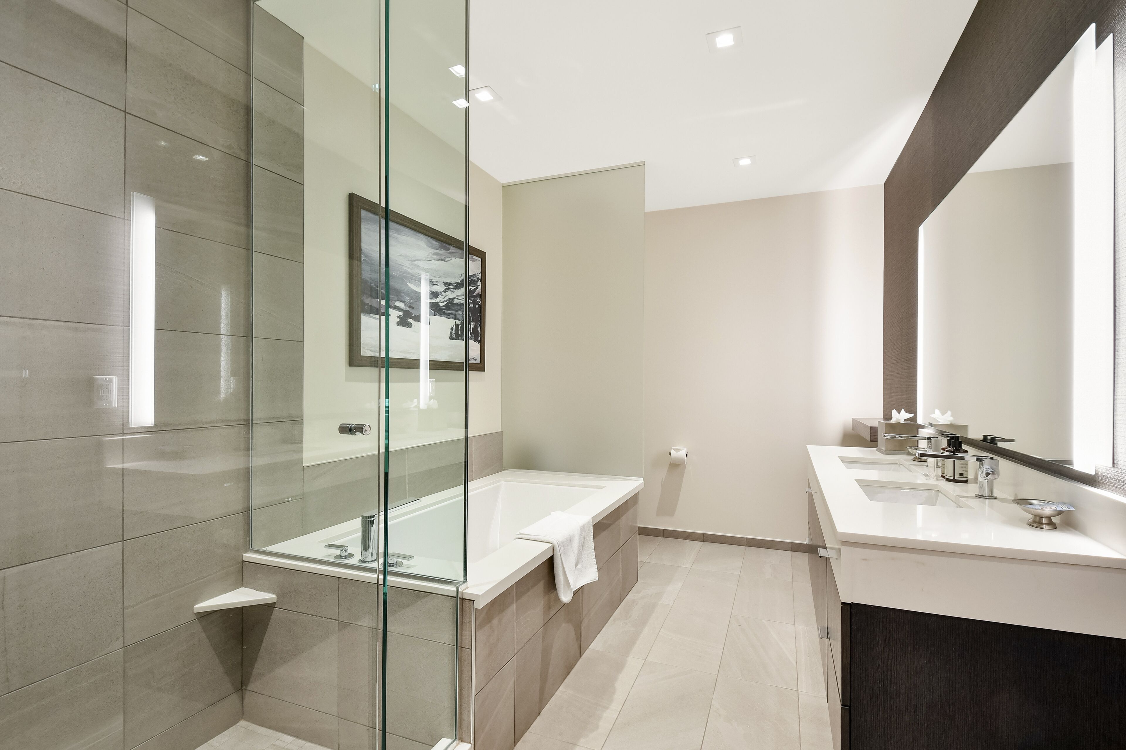 A modern bathroom with a glass shower enclosure, a bathtub, and a vanity with a large mirror.