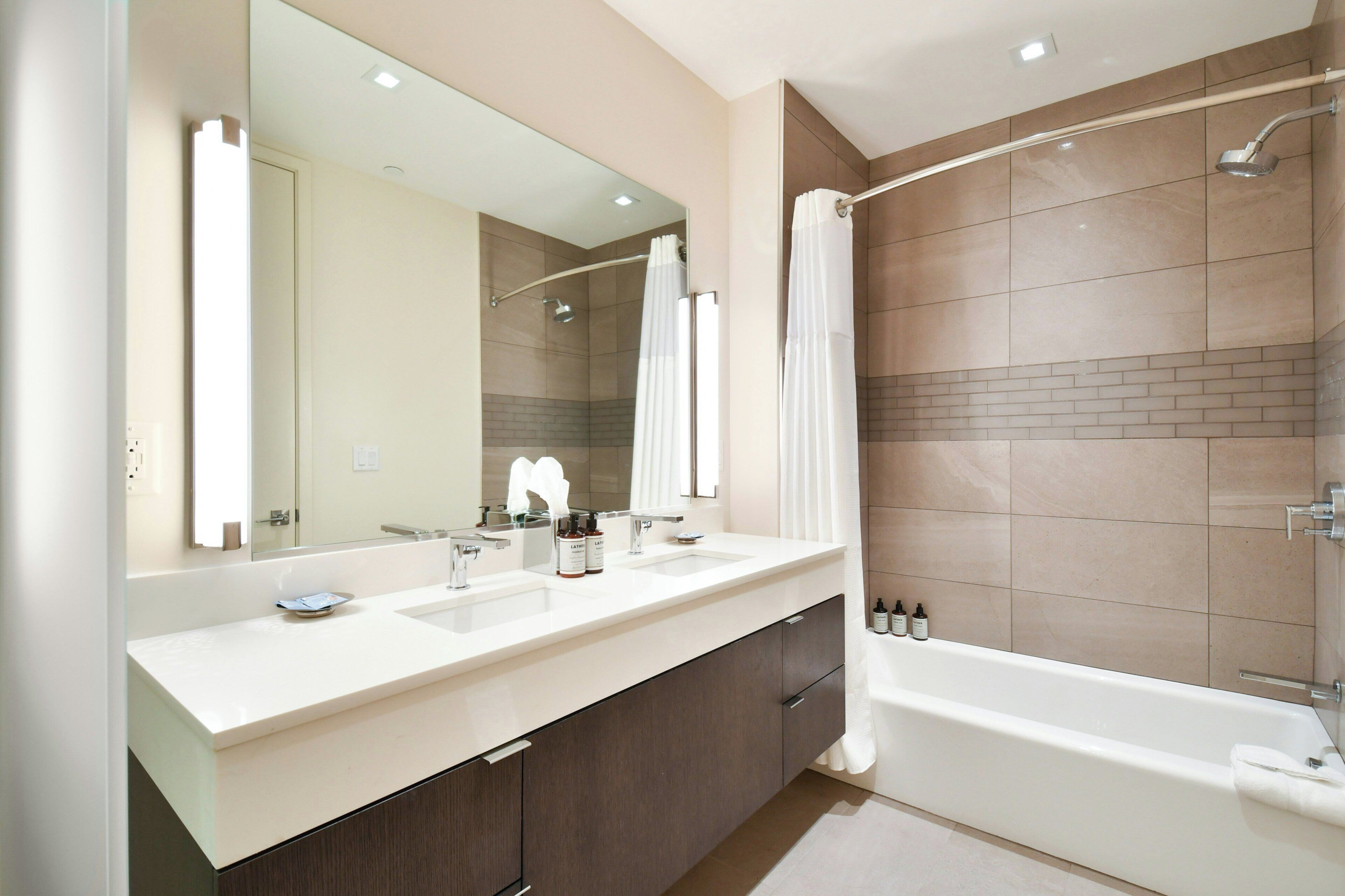 A modern bathroom with a large mirror, two sinks, a bathtub, and a shower area.