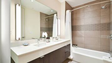 A modern bathroom with a large mirror, two sinks, a bathtub, and a shower area.