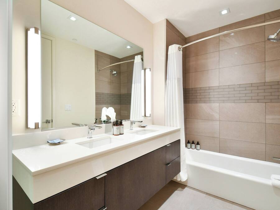 A modern bathroom with a large mirror, two sinks, a bathtub, and a shower area.