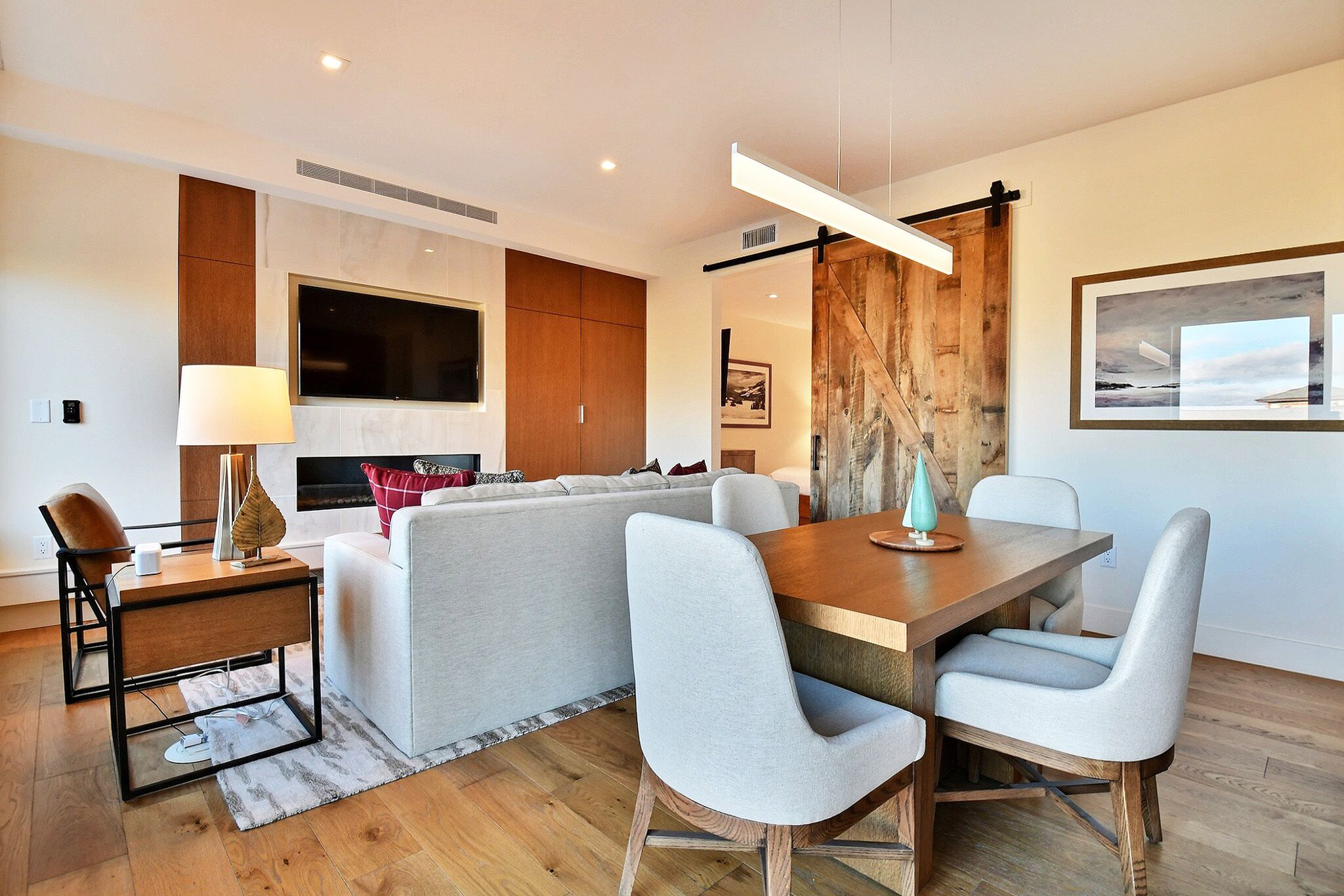 Una sala de estar moderna con un sofá, una mesa de comedor con sillas, un televisor montado en la pared y una pared de acento de madera.