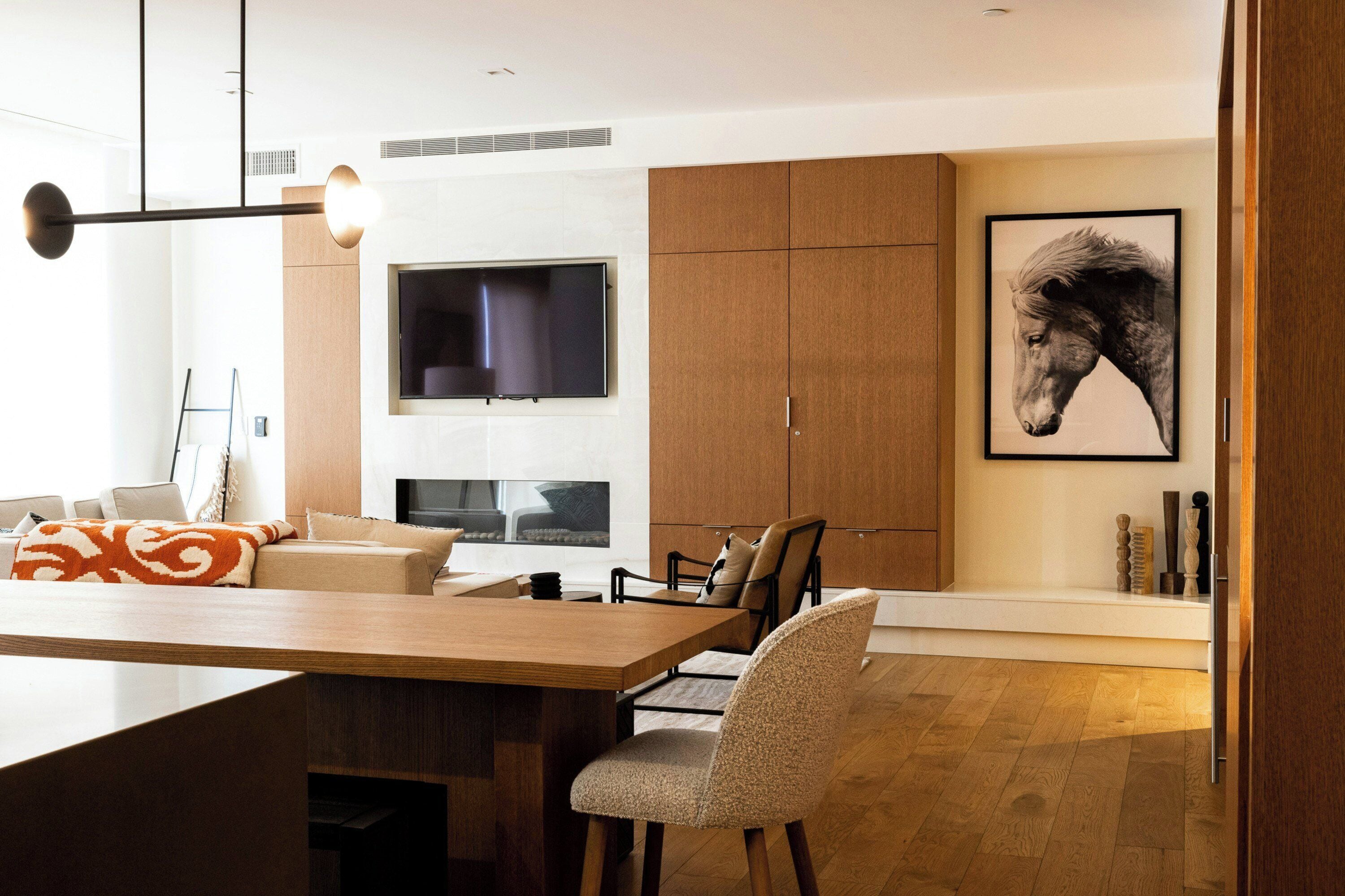 A modern living room with a wooden dining table, a sofa, and a TV mounted on the wall.