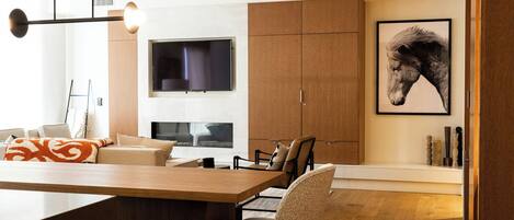 A modern living room with a wooden dining table, a sofa, and a TV mounted on the wall.