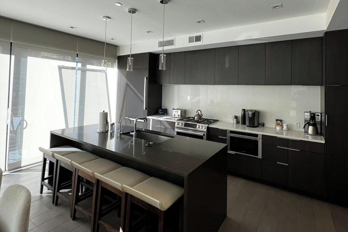 Una cocina moderna con una isla central, muebles oscuros y electrodomésticos de acero inoxidable.