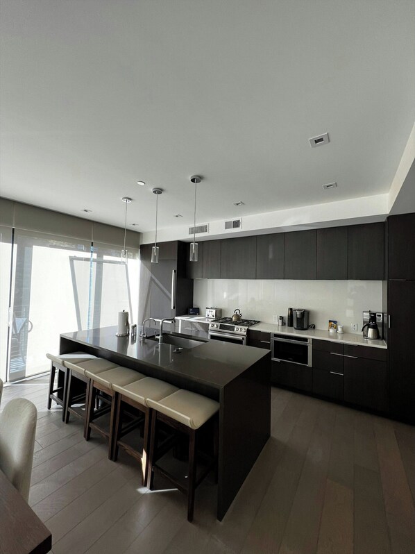 Una cocina moderna con una isla central, muebles oscuros y electrodomésticos de acero inoxidable.