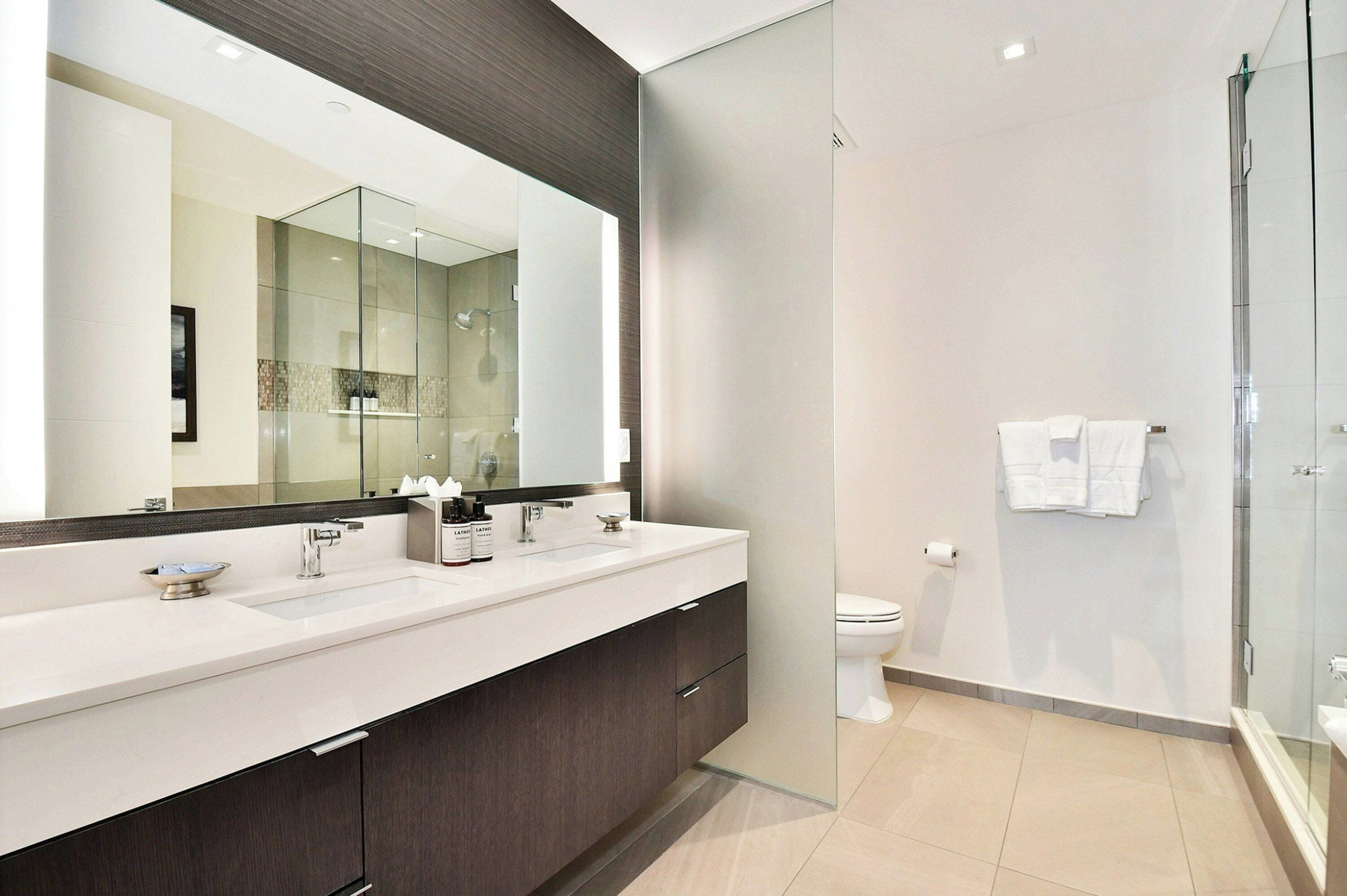 Un baño moderno con un espejo grande, una cabina de ducha de vidrio y un inodoro blanco.