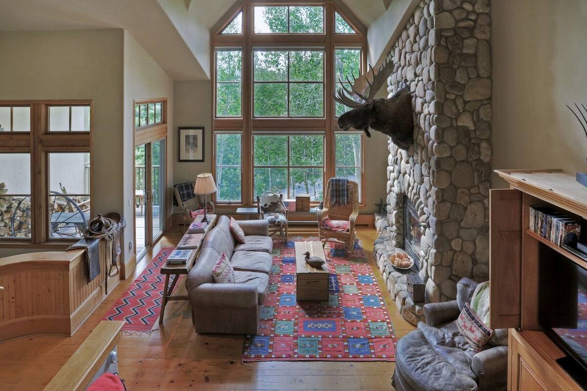A spacious living room with a stone fireplace, large windows, and a cozy seating area.