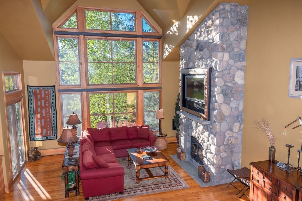 A spacious living room with a stone fireplace, large windows, and a red sofa.