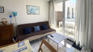 A living room with a sofa, a small table, a lamp, and a painting on the wall. - Cozy Apt with Terrace, 100m from St-Guirec Beach - Ploumanac'h (Perros-Guirec)