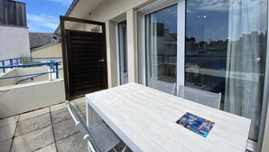 A balcony with a table and chairs, a sliding glass door, and a view of the cityscape. - Cozy Apt with Terrace, 100m from St-Guirec Beach - Ploumanac'h (Perros-Guirec)