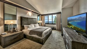 Habitación de hotel moderna con una cama grande, televisión, mesita de noche y vista al mar.