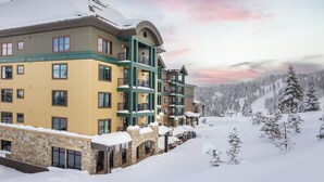 Un hotel de varios pisos con fachada de piedra, balcones y vistas a un paisaje nevado.