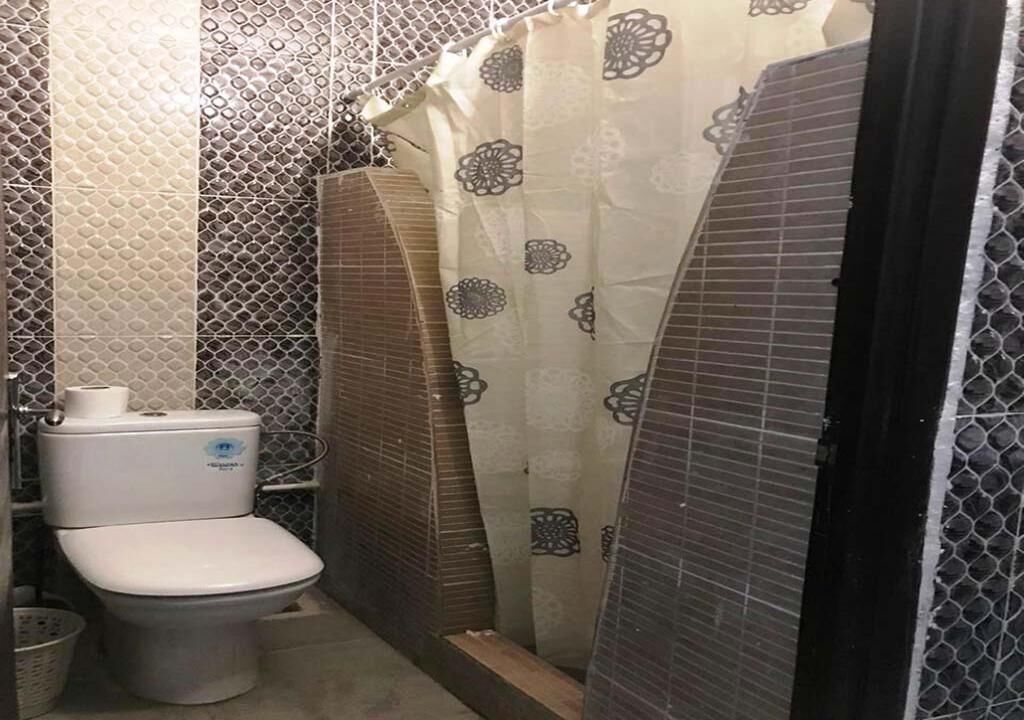 Een kleine, praktische badkamer met toilet, douchecabine en betegelde wanden.