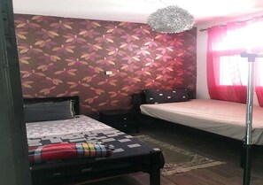 Une chambre à coucher comprenant un lit, une table de chevet, une commode, un luminaire suspendu et une fenêtre avec des rideaux rouges.