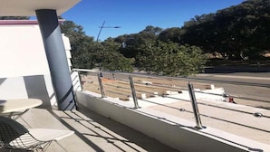 A balcony with a table and chairs, a hanging light fixture, and a view of a road with trees and a streetlight. - Residence Sogator 2382 (Saidia)