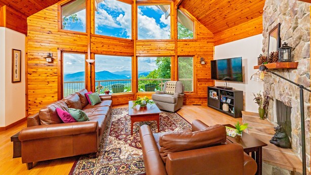 A spacious living room with a large wooden ceiling, a stone fireplace, and a television. - Mountain Lure: VIEWS OF BLUE RIDGE MTNS & LAKE LURE - NEAR ASHEVILLE & BLACK MTN (Old Fort)