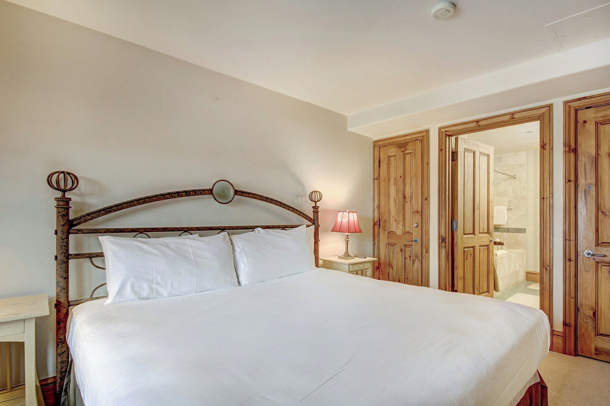 A neatly made bed with white linens, a wooden headboard, and a bedside lamp.