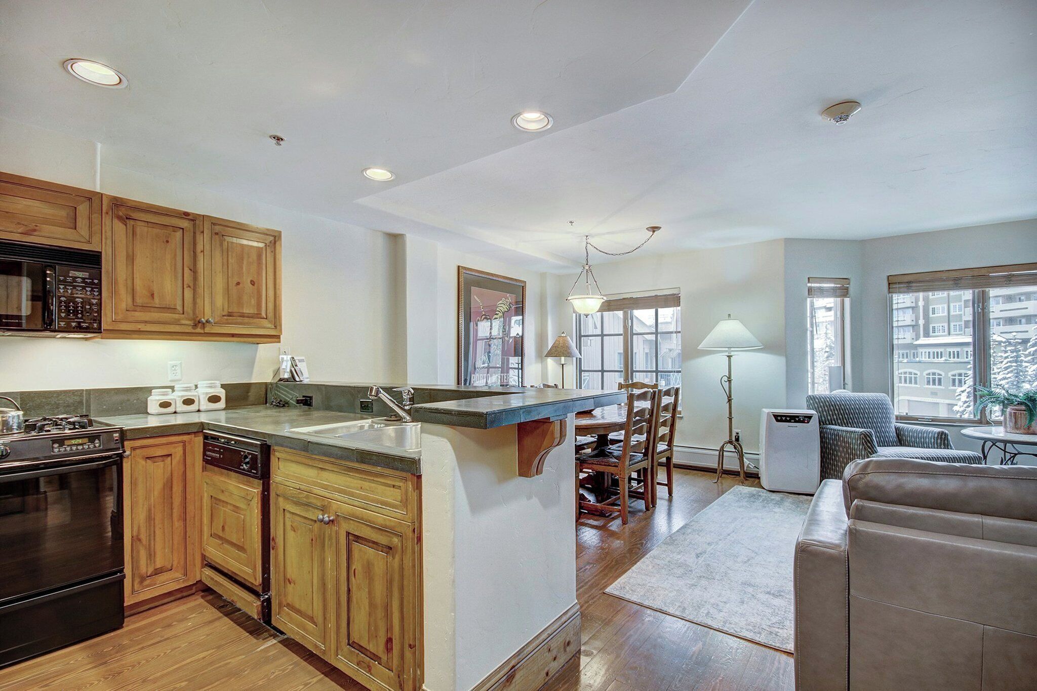 A kitchen with wooden cabinets, a built-in microwave, and a stove. There is a dining area with a table and chairs, and a sofa.