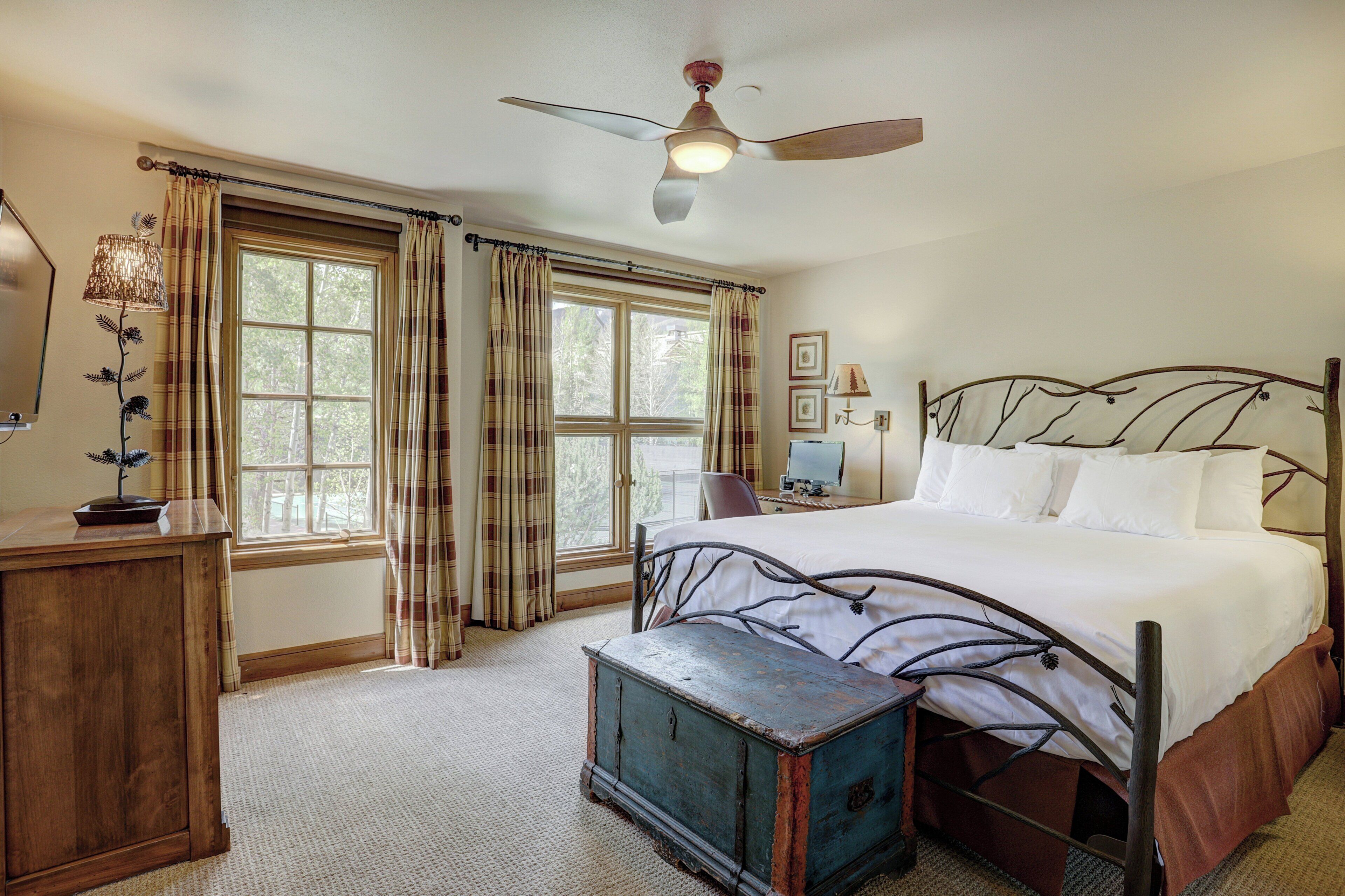 A bedroom with a bed, a wooden desk, a blue chest, and a ceiling fan.