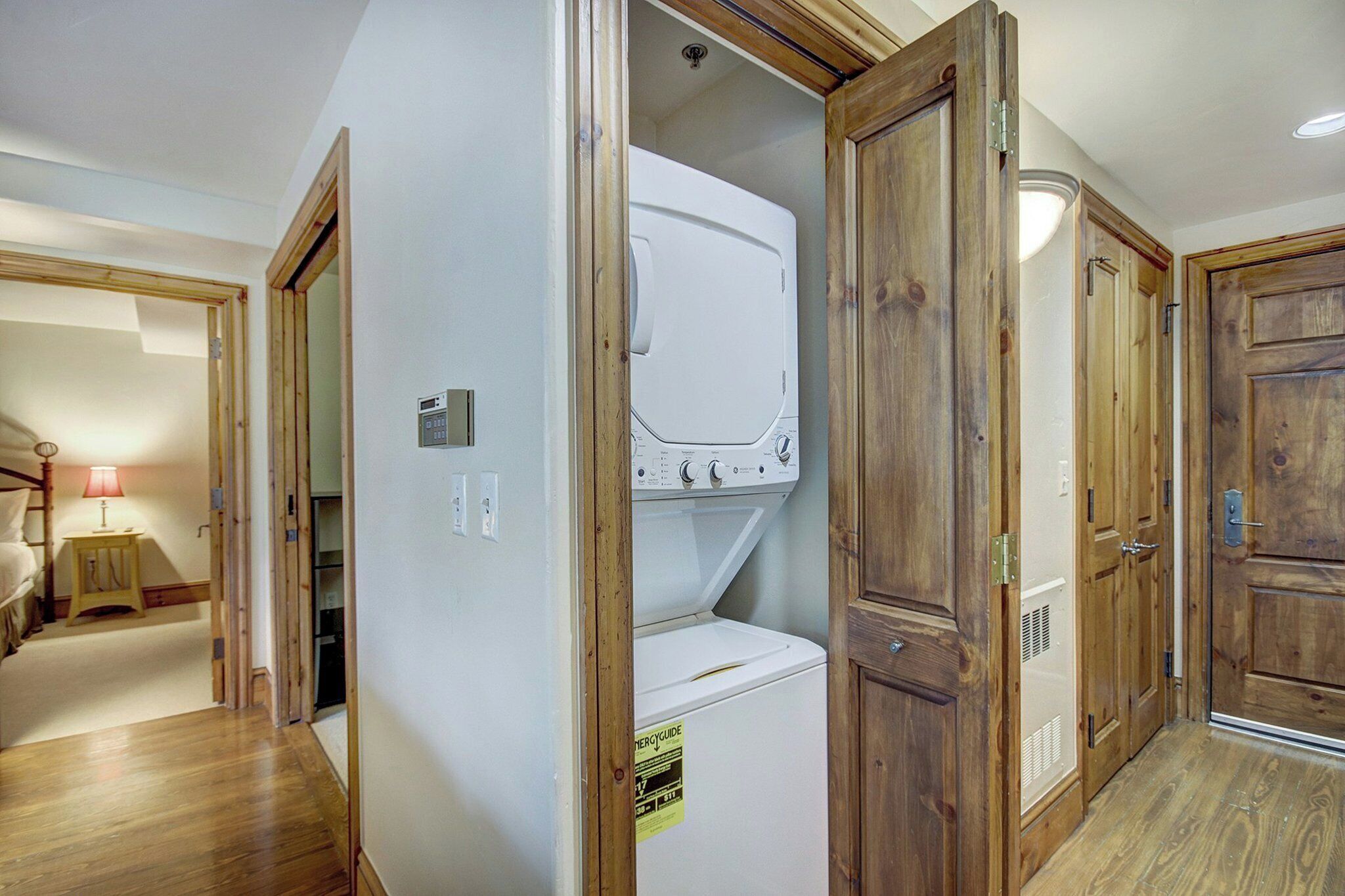 A laundry room with a front-loading washer and dryer, wooden doors, and a small table with a lamp.