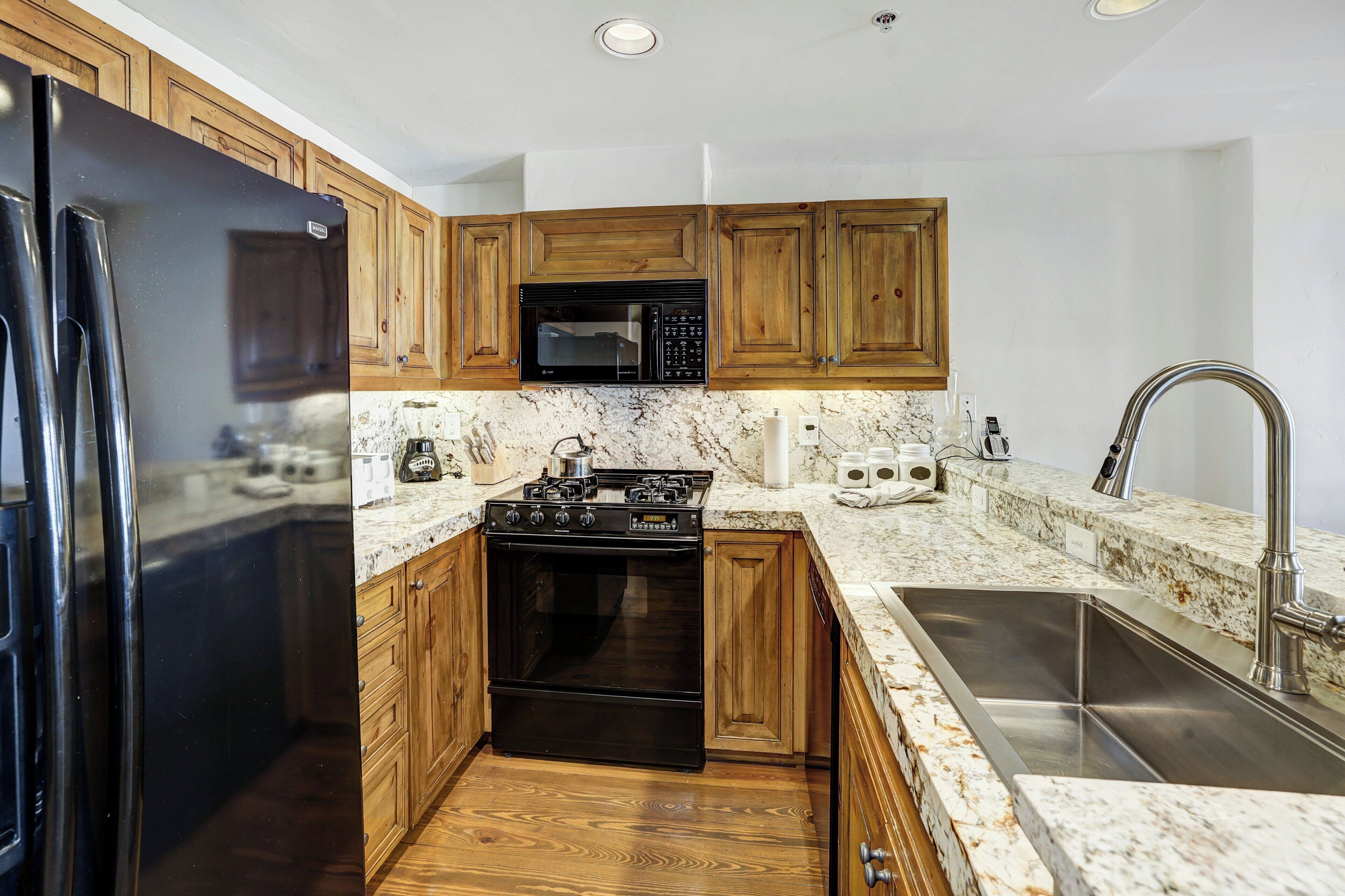 A kitchen with wooden cabinets, a black refrigerator, a microwave, a stove, and a sink.