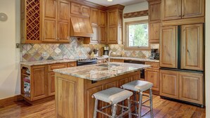 A kitchen with wooden cabinets, a large island with stools, a wine rack, and a tiled backsplash. - Beaver Creek Village by Vail Resorts (Avon)