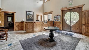 A reception area with a wooden reception desk, a round table with a glass top, a framed picture on the wall, and a heart-shaped glass door. - Beaver Creek Village by Vail Resorts (Avon)