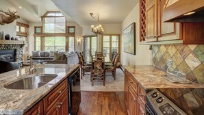 A spacious kitchen with a large island, wooden cabinets, and a stone fireplace. - Beaver Creek Village by Vail Resorts (Avon)
