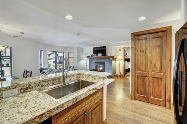 A modern kitchen with a granite countertop, stainless steel sink, wooden cabinets, and a fireplace. - Beaver Creek Village by Vail Resorts (Avon)