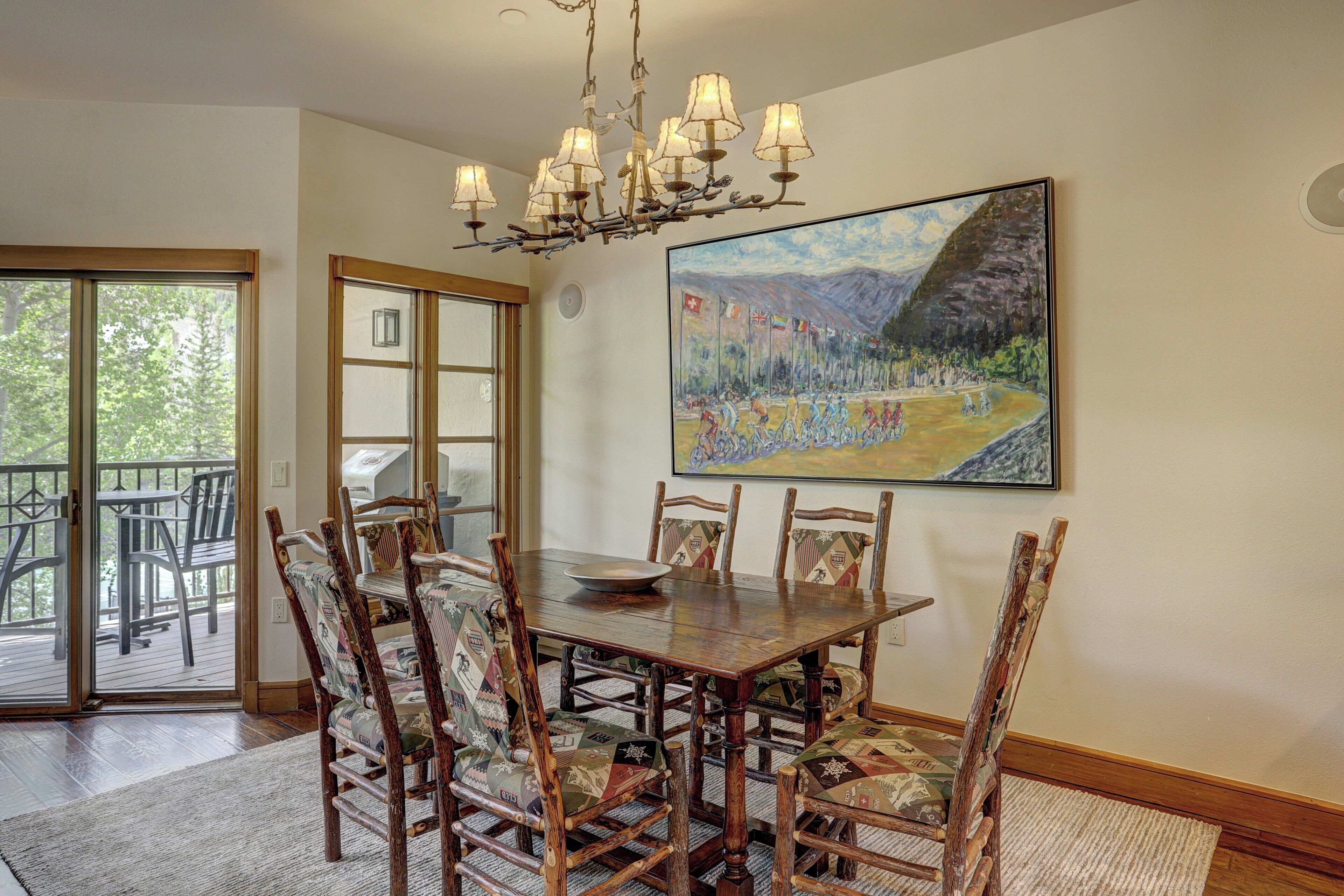 A dining area with a wooden table and chairs, a chandelier, and a painting on the wall.