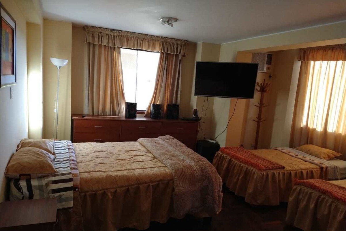 A hotel room with two beds, a TV, a desk, and a window with curtains.