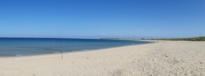 Une plage avec une canne à pêche plantée dans le sable, un ciel bleu dégagé et une mer calme.