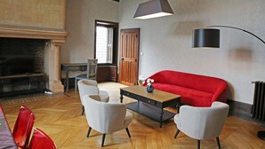 Una sala de estar con un sofá rojo, dos sillones estampados, una mesa de centro de madera, una chimenea y una lámpara colgante moderna.