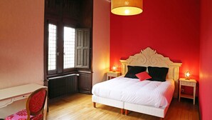 Un dormitorio con cama blanca, paredes rojas y suelo de madera.