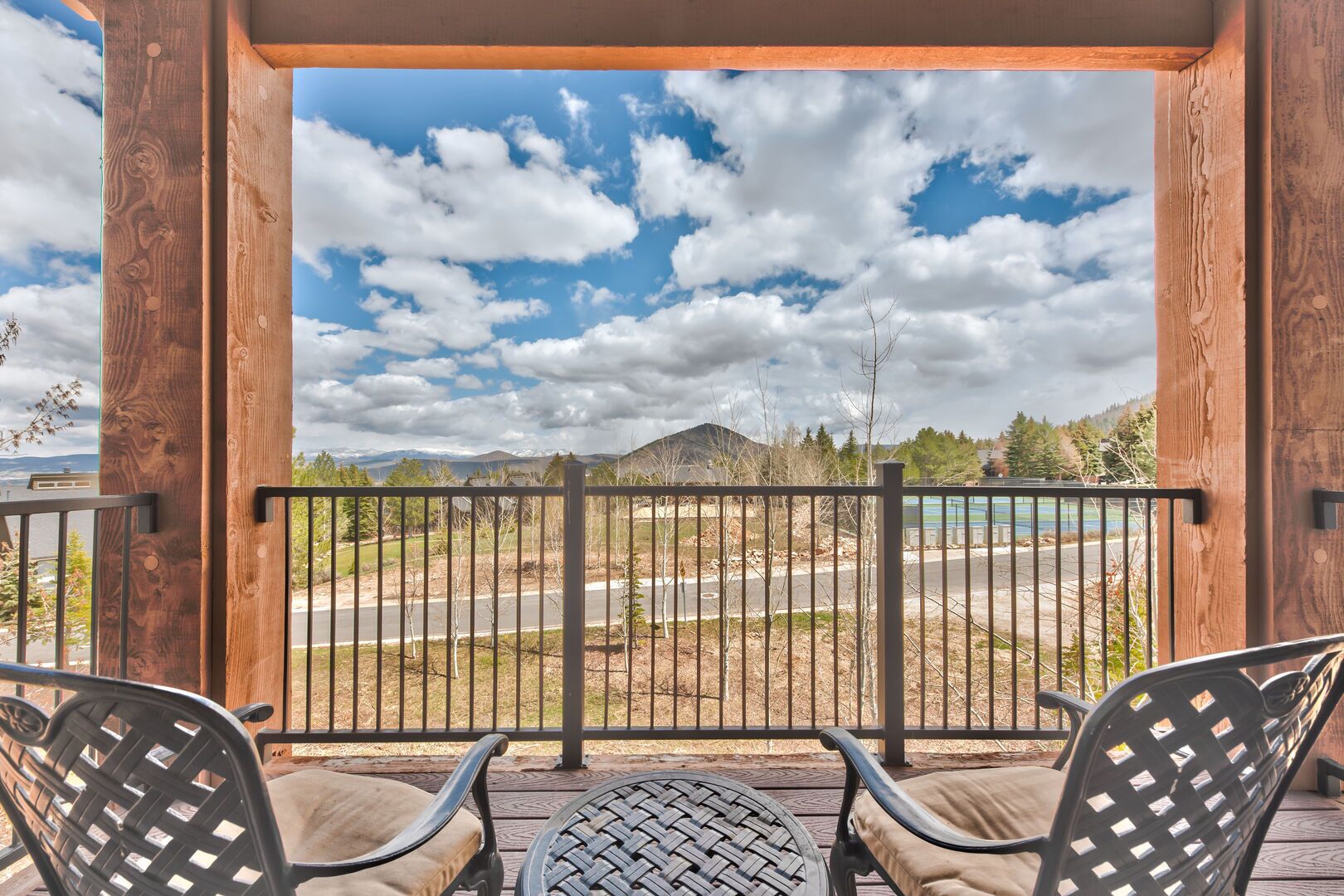 A balcony with two chairs and a table, overlooking a road and mountains.
