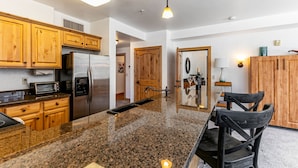 A kitchen with wooden cabinets, a stainless steel refrigerator, a granite countertop, and a black chair. - Resort property, corner one bedroom, pool, steps to skiing and golf, enjoy SV413B/C (Park City)