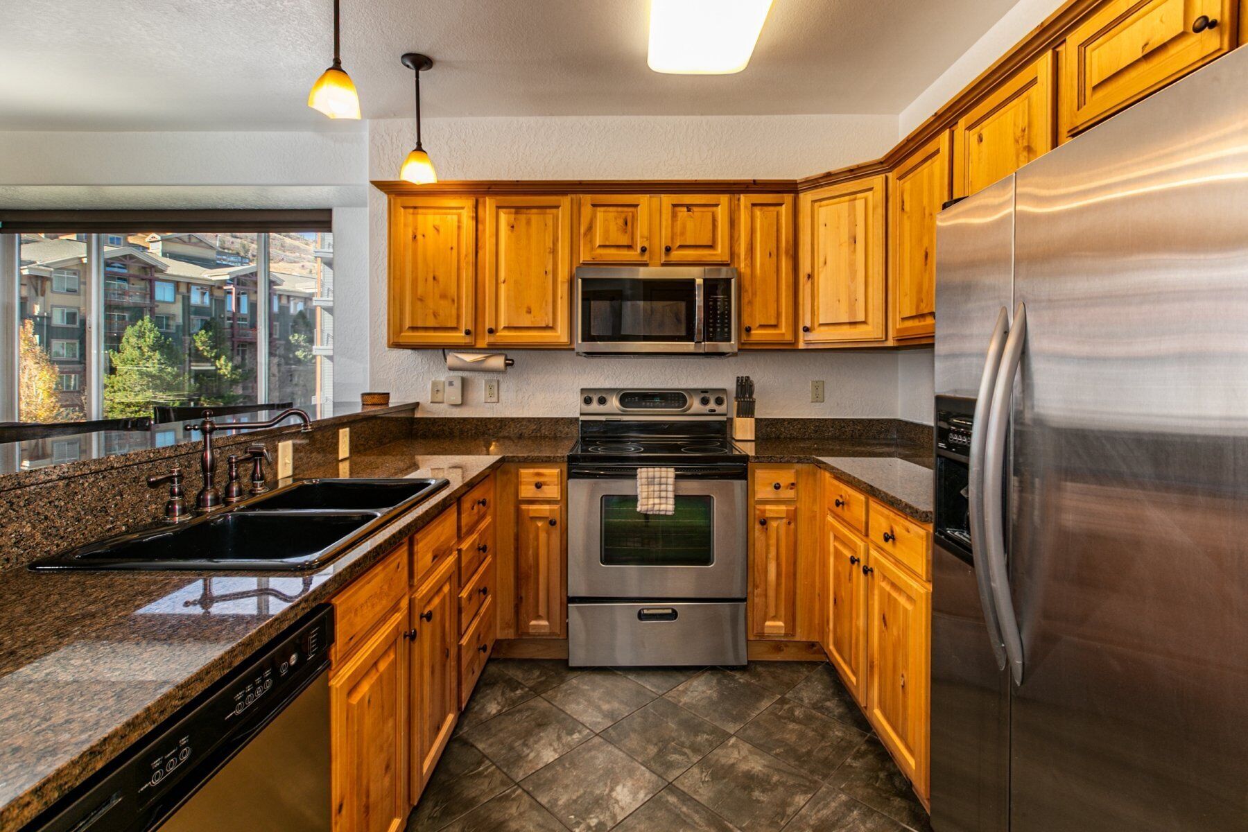 A modern kitchen with wooden cabinets, stainless steel appliances, granite countertops, and a large window offering a view of the city.
