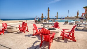 Ein Poolbereich mit roten Adirondack-Stühlen, einer Feuerstelle und Sonnenschirmen.