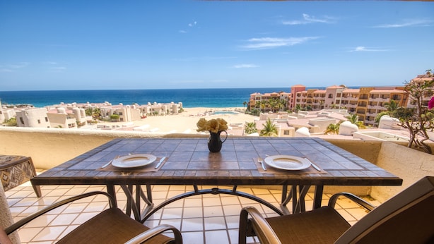 Ein Esstisch mit Stühlen und einem Blumenstrauß, mit Blick auf einen Strand und das Meer.