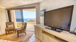 Ein Zimmer mit einem großen Flachbildfernseher, einem Sessel, einem kleinen Teppich und Meerblick durch eine Schiebetür.