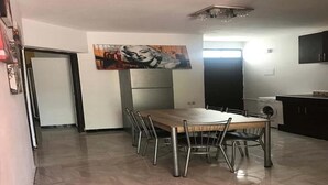 Een eetruimte met een houten tafel en metalen stoelen, een groot schilderij aan de muur, en een keuken met kasten en een wasmachine.
