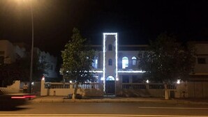 A building with a prominent vertical light structure in front, surrounded by trees and a fence. - Residence Sogator 4124 (Saidia)