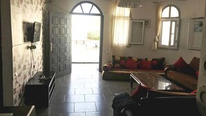 A living room with a sofa, a coffee table, and a TV mounted on the wall. There is a door leading to an outdoor area. - Residence Sogator 4124 (Saidia)
