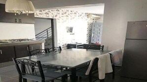 A modern kitchen with a dining area, featuring a large table, chairs, a refrigerator, and a staircase leading to an upper level. - Residence Sogator 4124 (Saidia)