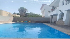 A swimming pool with a tiled deck, a white building with balconies, and a palm tree in the background. - Residence Sogator 4124 (Saidia)