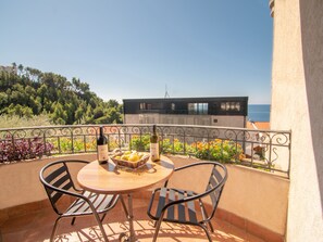 A balcony with a round table, two chairs, a bottle of wine, and a basket of lemons. - Levantin Inn half Room N7 Sea Side (Sveti Stefan)