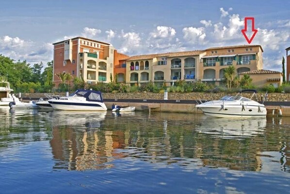 Un port de plaisance où sont amarrés plusieurs bateaux, un immeuble à plusieurs étages doté de balcons et un ciel dégagé.