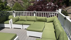 Une terrasse dotée d’une balustrade blanche et de coussins verts sur un canapé en osier blanc.