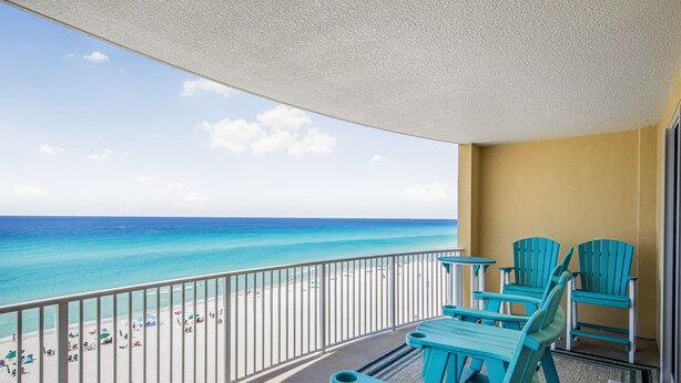 A balcony with a view of the beach and ocean, turquoise chairs, and a yellow wall.